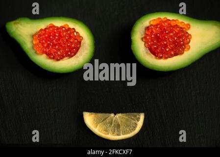 Caviar rouge en tranches d'avocat et une tranche de citron sur fond noir. Fruits et caviar sous forme de visage souriant. Mise au point sélective. Le concept Banque D'Images