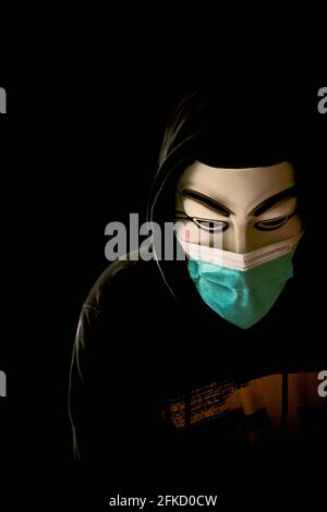 Homme portant un masque Vendetta et un masque médical isolé sur le noir. Banque D'Images