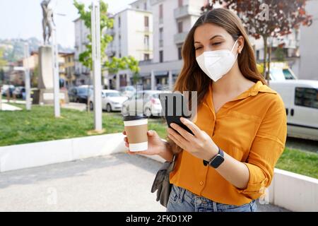 Femme d'affaires avec KN95 FFP2 masque de visage en utilisant des poignées de smartphone tasse de café en papier dans la rue de la ville Banque D'Images