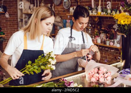 Femme fleuriste avec assistant collectent des bouquets dans un fleuriste. Banque D'Images