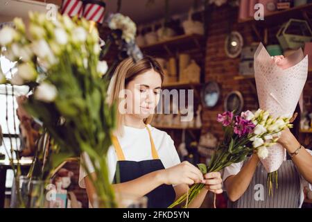 Femme fleuriste avec assistant collectent des bouquets dans un fleuriste. Banque D'Images