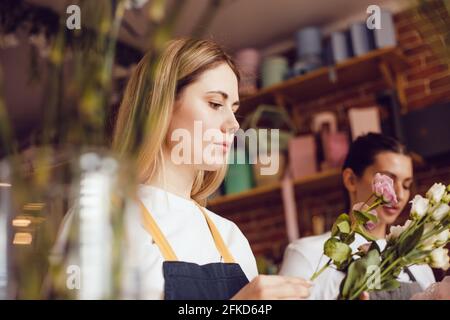 Femme fleuriste avec assistant collectent des bouquets dans un fleuriste. Banque D'Images