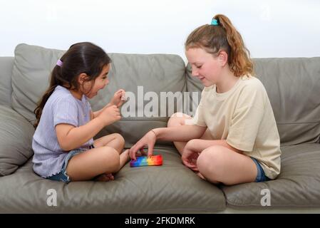Deux enfants adorables jouant avec le violon Pop IT. Une fille riante lève les mains dans la victoire. Pousser pop bulle flexible violon jouet sensoriel fournir décharge et sont bons pour le développement de l'enfant. Banque D'Images