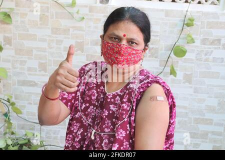 Femme indienne faire le pouce après avoir obtenu la vaccination pendant la nouvelle souche de covid-19, la femme mature portant un masque avec bandage appliqué a reçu un coronavir Banque D'Images