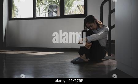 Jeune femme solitaire assise sur le sol dans une pièce sombre avec sentiment de tristesse et de dépression. Banque D'Images