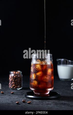 Café glacé versé dans un grand verre sur fond sombre. Concept boisson rafraîchissante d'été. Banque D'Images