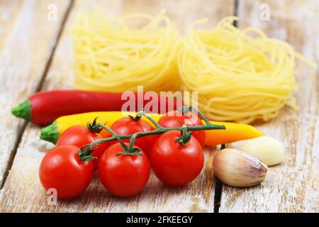 Sélection d'ingrédients de cuisine : tagliatelle, tomates cerises, gousses d'ail et piments sur une surface en bois Banque D'Images