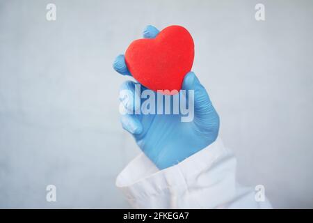 homme main dans des gants de protection tenant coeur rouge sur blanc arrière-plan Banque D'Images