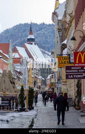 Les amateurs de shopping au milieu de la neige de printemps à Strada Republicii, dans le centre historique de Brasov en Roumanie. La célèbre église noire est importante en arrière-plan - pH Banque D'Images