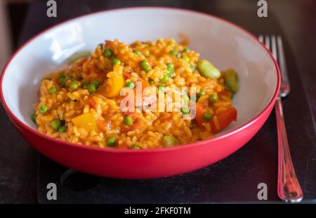 Gros plan sur une paella de légumes maison saine et nutritive dans un saladier rouge avec mise au point sélective, faible profondeur de champ et bokeh Banque D'Images