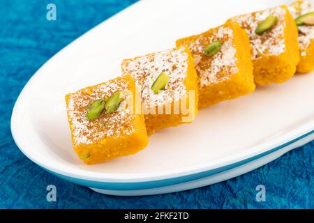 Vue de dessus de délicieux Mithai Moong Dal Burfi ou Meetha Mung Daal Barfi Barfee cuisiné à Desi ghee mélangé avec Mawa et Pistachio dans le plateau blanc. Banque D'Images