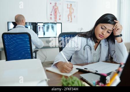 Cardiologue indien fatigué décrivant le cardiogramme du patient et de la prise notes dans le document Banque D'Images