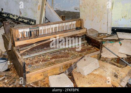 Un vieux piano cassé et fortement endommagé entouré de débris qui se trouvent sur le plancher d'un bâtiment abandonné. Banque D'Images