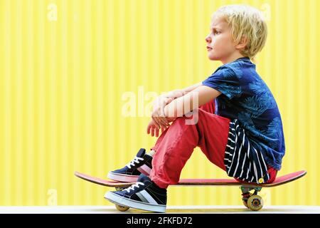 Un petit skater avec skateboard s'amuser avant la formation des enfants dans le parc de skate. Style de vie familial actif, activités de loisirs en plein air Banque D'Images