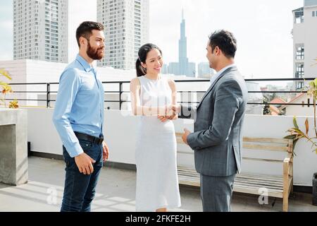 Souriante, jolie femme d'affaires asiatique se mêlant à un partenaire d'affaires indien lors d'une réunion sur le toit lors d'une réunion de la société internationale Banque D'Images