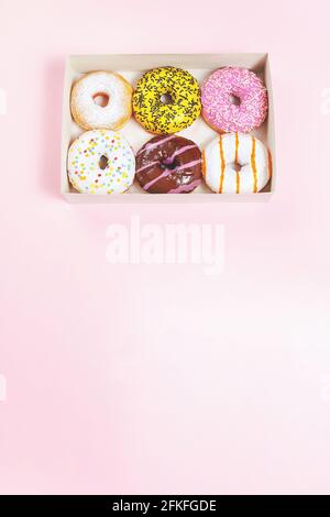 Boîte à beignets. Un ensemble ou un assortiment de beignets glacés de couleur avec des arrosettes et de la garniture. Fond rose. Délicieux en-cas ou dessert. Différentes saveurs Banque D'Images