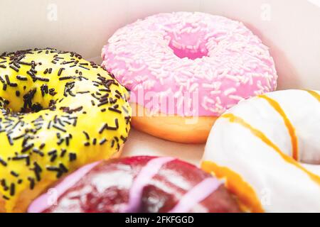 Gros plan sur les beignets ronds de couleur avec des arrosettes et de la garniture. Boîte à beignets émaillée. Fond rose pastel. Beignets aux saveurs différentes - caramel Banque D'Images