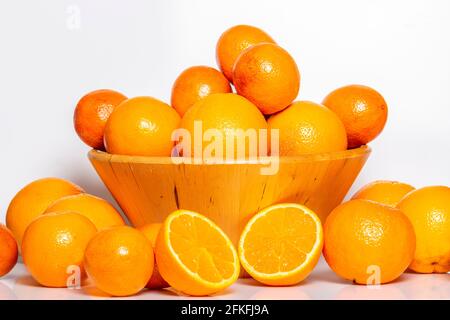 de nombreuses oranges se trouvent sur un fond blanc à côté d'un bol avec beaucoup d'oranges Banque D'Images