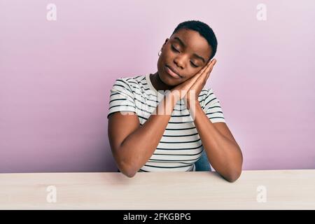 Jeune femme afro-américaine portant des vêtements décontractés assis sur le table dormant fatigué rêvant et posant avec les mains ensemble pendant souriant avec du clo Banque D'Images