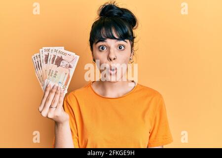 Une jeune fille hispanique détenant 5000 sud-coréennes a gagné des billets effrayés et étonnés par la bouche ouverte pour la surprise, le visage incrédulé Banque D'Images