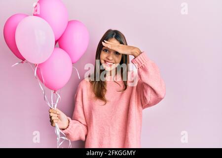 Jeune femme brune tenant des ballons roses stressés et frustrés avec la main sur la tête, surpris et fâché visage Banque D'Images