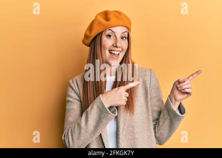 Jeune femme irlandaise portant un regard français avec un béret souriant et regardant la caméra pointant avec deux mains et des doigts sur le côté. Banque D'Images