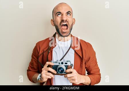 Un jeune homme hispanique tenant un appareil photo d'époque en colère et fou criant frustré et furieux, criant avec colère regardant vers le haut. Banque D'Images