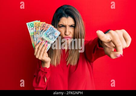Belle femme brune tenant des dollars australiens pointant mécontent et frustré à la caméra, en colère et furieux avec vous Banque D'Images