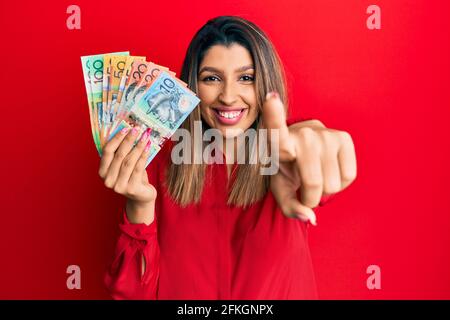 Belle femme brune tenant des dollars australiens pointant vers vous et la caméra avec les doigts, souriant positif et gai Banque D'Images