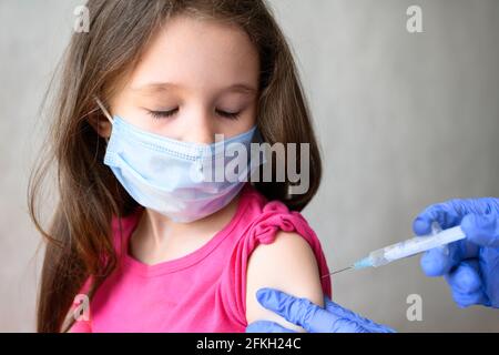 Vaccination de l'enfant de COVID-19 ou de la grippe, petite fille mignonne dans le masque ferme les yeux pendant l'injection. Le médecin tient la seringue pour jab à l'enfant. Concept de coro Banque D'Images