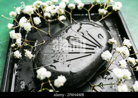 Aiguilles d'acupuncture, pierre thermale et fleurs sur le support Banque D'Images