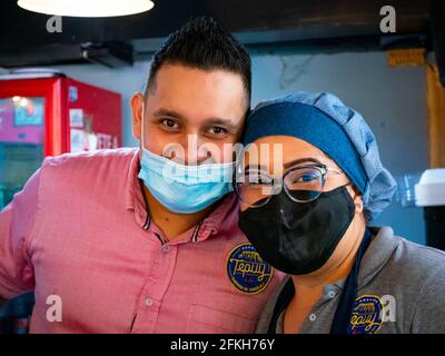 Medellin, Colombie - Mars 28 2021: Jeune latins portant un masque bleu sous son nez à côté d'une femme Brunette portant un uniforme et un masque noir Banque D'Images