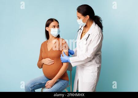 Médecin généraliste vaccinant la patiente enceinte contre le coronavirus, fond bleu Banque D'Images