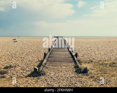 Promenade en bois avec des intempéries ou chemin menant à la plage de galets à la mer à distance. Banque D'Images