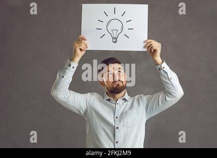 Jeune homme tenant une photo d'une ampoule, pensant et considérant une idée novatrice intéressante Banque D'Images
