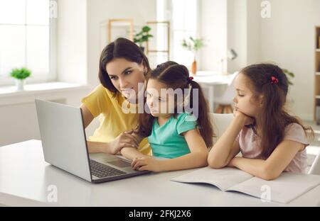 Jeune mère de race blanche avec deux petites filles faisant leurs devoirs à l'aide de ordinateur portable Banque D'Images