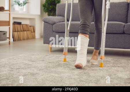 Le patient dont la jambe est cassée en fonte se tient debout du canapé et marche à la maison en utilisant des béquilles Banque D'Images