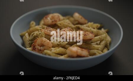 pesto penne avec crevettes frites dans un bol bleu sur fond noir, photo large Banque D'Images