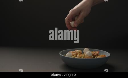 main d'homme ajouter des boules de mozzarella au pesto penne avec des crevettes frites dans un bol bleu sur fond noir, photo large Banque D'Images