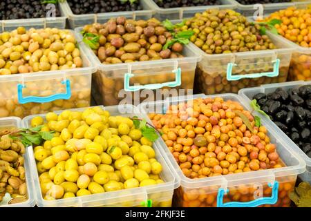 Plusieurs récipients en plastique avec pile d'olives grecques mixtes biologiques mûres (noir, vert, jaune) dans l'huile sur le stand d'exposition dans l'épicerie / supermarché Banque D'Images