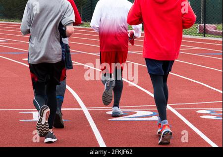 Vue arrière de quatre coureurs d'école secondaire qui s'exécutent sur une piste traversant la ligne d'arrivée ensemble dans un groupe pendant la course et le champ. Banque D'Images