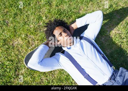 Homme d'affaires noir couché sur l'herbe avec son skateboard Banque D'Images