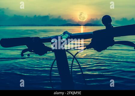 Silhouette d'un vélo de pièces, guidon sur la plage contre la pleine lune lumineuse dans la mer. Réflexion de la lune dans l'eau. À l'extérieur. Cross Process et vi Banque D'Images