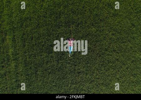 Vue aérienne d'une agricultrice qui se trouve dans un champ de blé vert et qui se repose, haut en bas drone pov de femme agronome dans le wheatgrass Banque D'Images