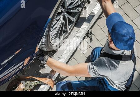 Un travailleur caucasien de remorquage automobile dans ses années 40 sécurisant la voiture sur son camion de remorquage. Thème de l'industrie du transport et de l'automobile. Banque D'Images