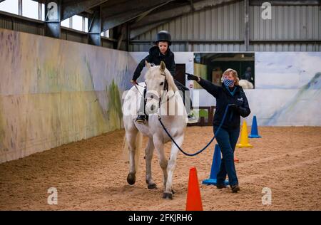 Garçon à cheval blanc apprenant contrôle de rein, équitation pour handicapés à Muirfield Riding Therapy, East Lothian, Écosse, Royaume-Uni Banque D'Images