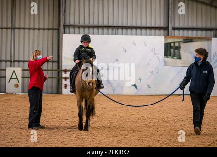 Garçon avec le syndrome de Down équitation avec entraîneur instruting, équitation pour handicapés à Muirfield Riding Therapy, East Lothian, Écosse, Royaume-Uni Banque D'Images