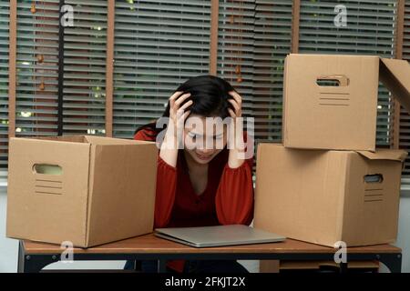 Triste femme asiatique emballage des effets dans une boîte en carton et pleurer sur le bureau après avoir été mise à pied et au chômage. Concept d'impact sur le Banque D'Images