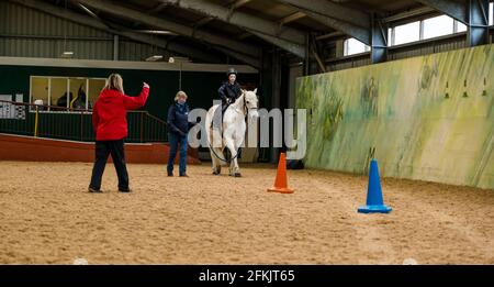 Garçon à cheval avec entraîneur instruting, équitation pour handicapés à Muirfield Riding Therapy, East Lothian, Écosse, Royaume-Uni Banque D'Images