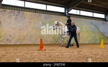 Garçon à cheval blanc apprenant contrôle de rein, équitation pour handicapés à Muirfield Riding Therapy, East Lothian, Écosse, Royaume-Uni Banque D'Images